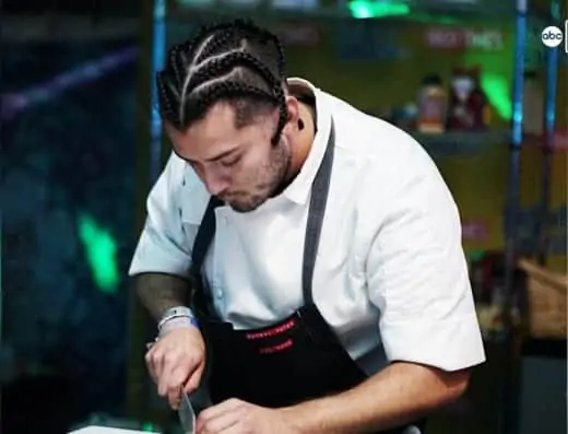 A chef expertly cuts a piece of meat with herbal notes on a plate.