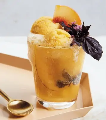 A delicious cbd infused peach and ginger alte float is neatly placed on a table with a purple garnish.