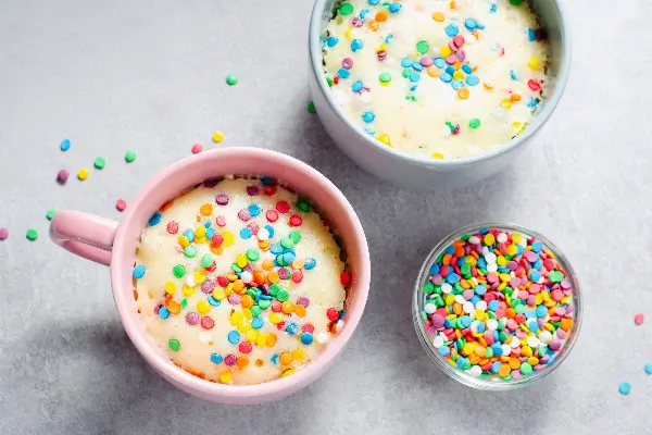 Two mugs of vanilla cannabis infused cake with rainbow confetti sprinkles.