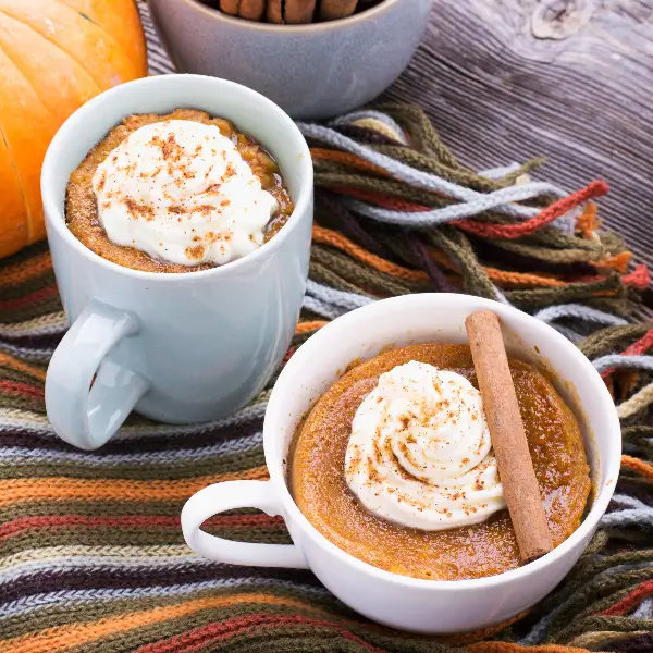 Two white mugs filled with cannabis infused pumpkin cake topped with whipped cream and cinnamon. 
