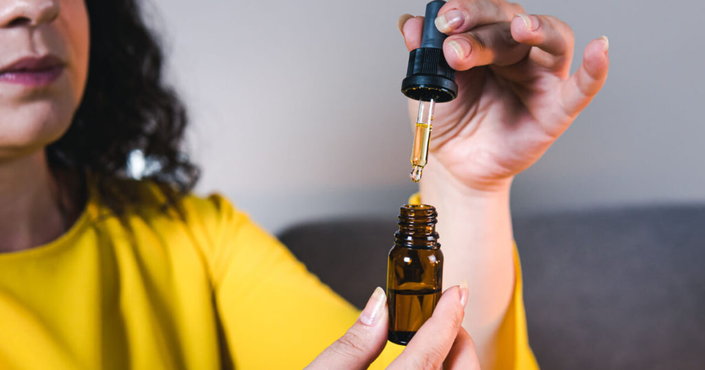 A medical cannabis caregiver in a bright yellow shirt measures out medical cannabis oil with a dropper. 