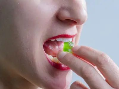 A woman with bright lipstck bites into a green THC cannabis gummy bear edible.