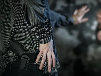 A man has a black handgun in the back of his pants while motioning to stop.