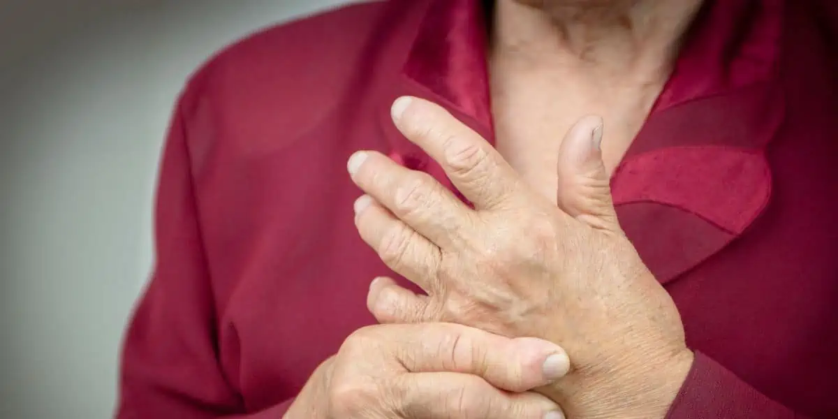 A woman in a red blouse massages her hand to alleviate pain from Rheumatoid Arthritis.