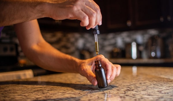A hand holding a dropper above a small glass bottle