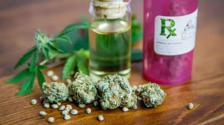 A pink bottle of medical marijuana, green bud, oil, and seeds are on a table.