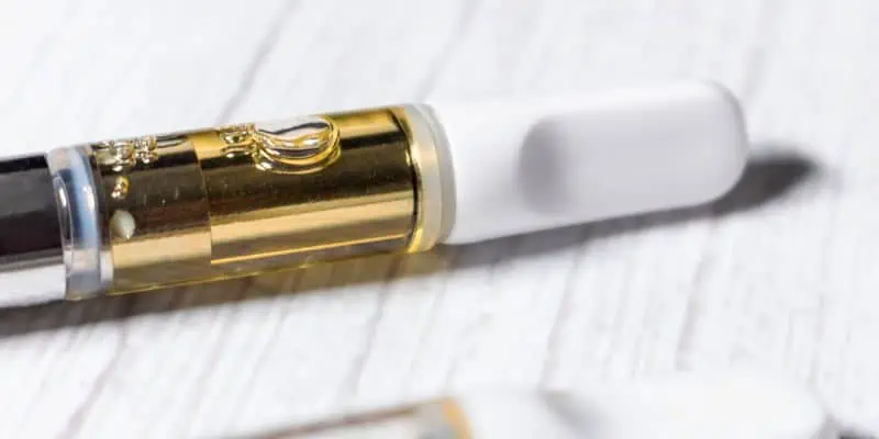 This photo shows a cannabis distillate vape pen with a white mouthpiece placed on a white wooden table.