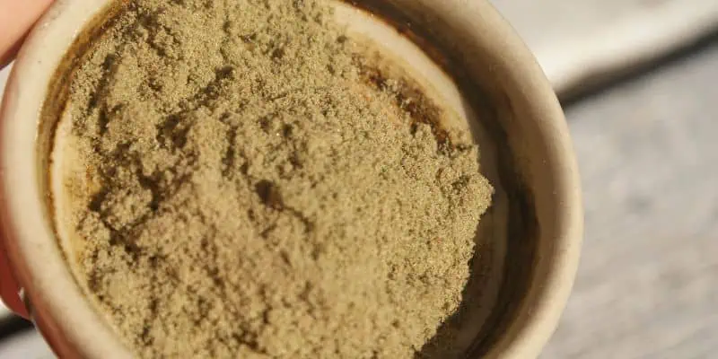 Held in a brown ceramic bowl, this photo features cannabis trichomes, known as kief, collected through a screen by sifting the cannabis flower.