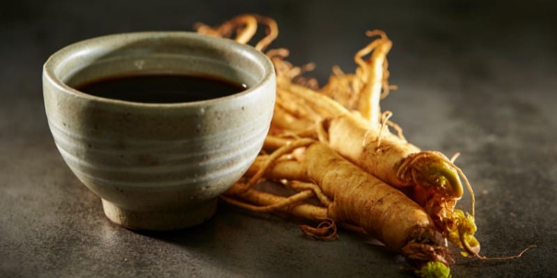 On a granite looking counter top, a cup of tea sits next to a ginseng root.