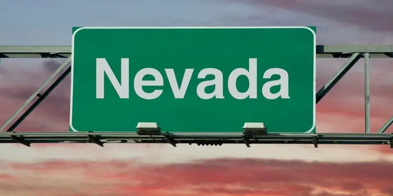 Looking at a high way sign against the sunset in the background, the image shows "Nevada" in the sign.