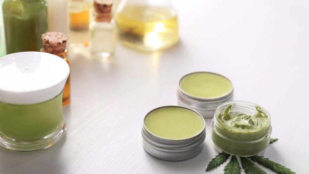 This image shows a handful of cannabis salves and balms on a table with other cannabis products.