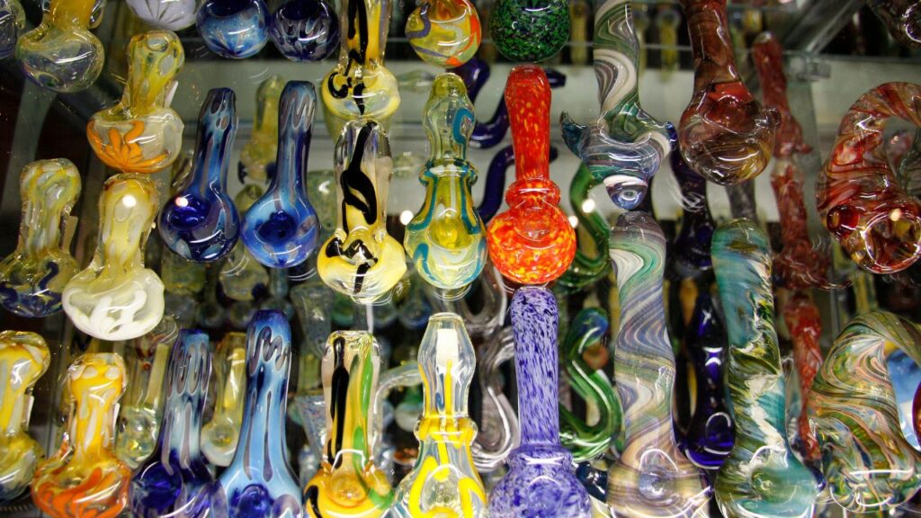 glass pipes are laid out on a glass table featuring a number of colorful hand pipes typically used for the consumption of cannabis
