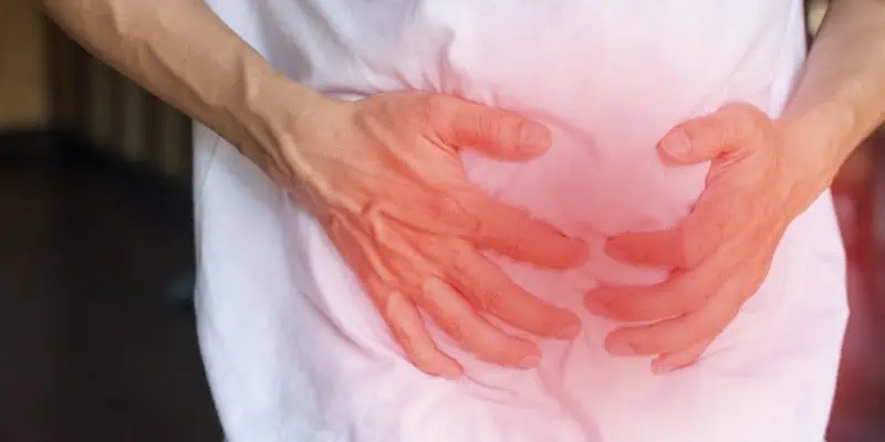 This photo shows a man in a white shirt holding his stomach with both hands and a red illuminating aura surrounding it, indicating the pain experienced from crohn's