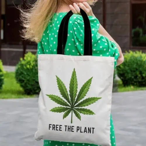 A woman in a green dress sports a cannabis tote bag that reads "free the plant" and a big green marijuana leaf above it.