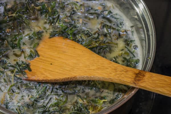 A close up of cannabis simmering in butter to infuse cannabis butter. A wood spoon is in the sauce pan.