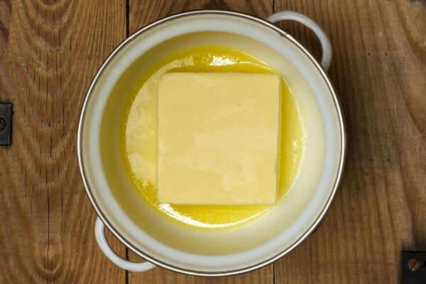 A white pan has a pound of butter in it half melted. This butter is being clarifiesd to make cannabis butter.