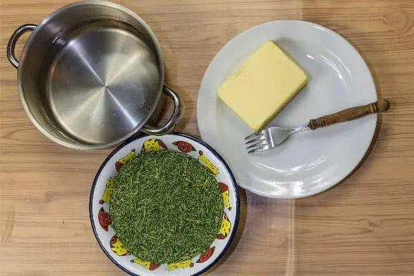 A saucepan, ground cannabis and butter are diplayed on a table to prepare for infusing cannabis butter.