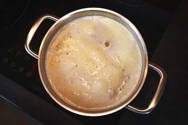 A pan of butter simmers on a stovetop to clarify butter. The white foam can be seen on top. 