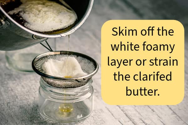 A pan of clarified butter is being strained through a cheesecloth and metal strainer. The white foam stays beind.