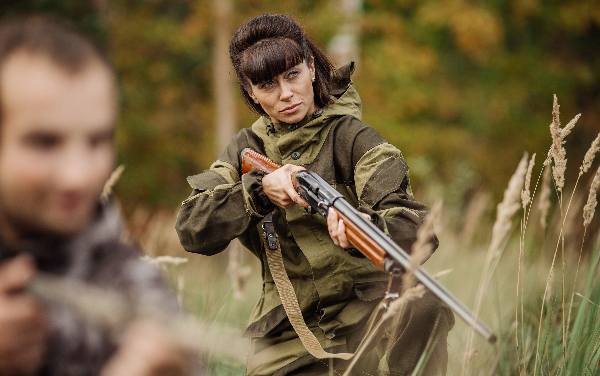 A woman holding a hunting rifle and a man holding a hunting shotgun.