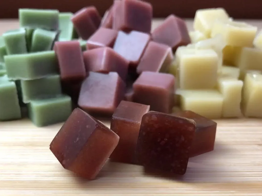 green, red, and off-white keto friendly edible gummies are piled high on a wood cutting board
