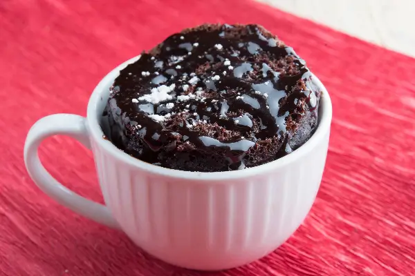 A white mug holda a baked chocolate cannabis infused mag cake dripping with hot fudge on top. 