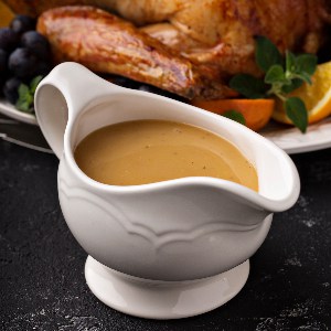 A boat of cannabis infused gravy on a black counter top with a delicious turkey next to it