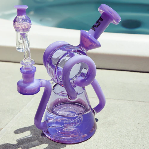 A purple glass water pipe with a complex design sits beside a swimming pool on a sunny day.