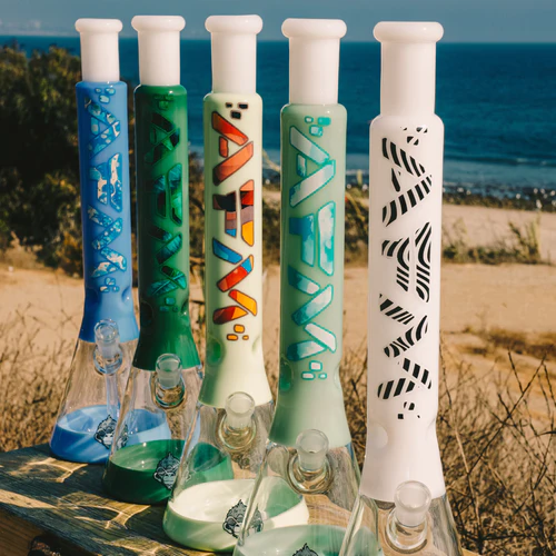 Four decorative bongs in various designs displayed on a wooden table against a beach background.