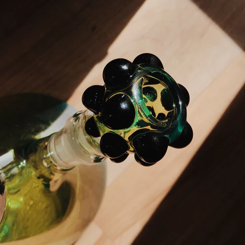 A glass wine stopper with black and green design, inserted in a bottle, casting a shadow on a wooden surface.