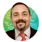 A smiling man with a short beard and mustache wearing a dark suit, white checkered shirt, and red tie. The background is a green and blue circular gradient with a subtle pattern.
